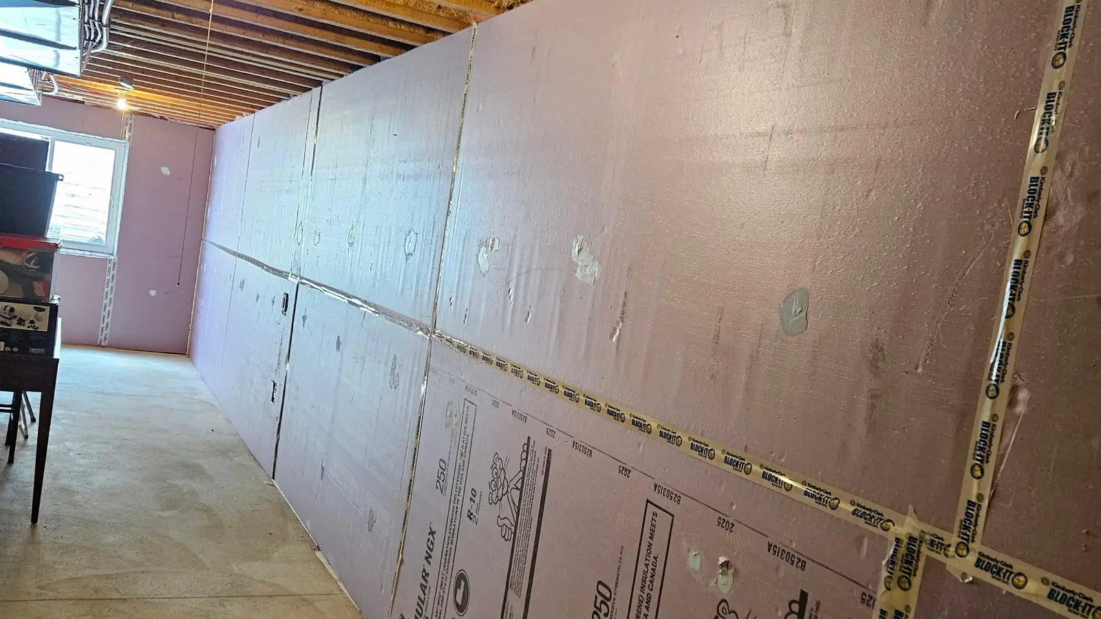 Long unfinished basement wall covered in pink foam board, with taped seams